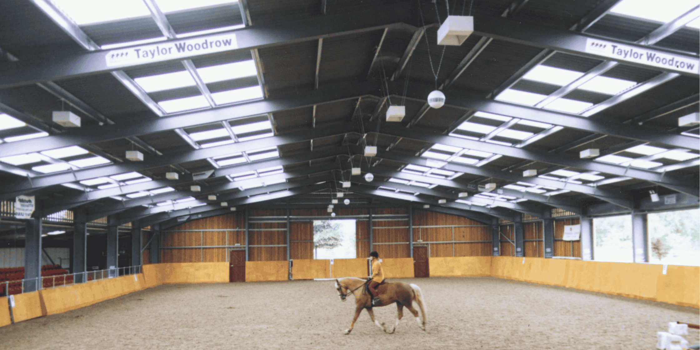 a person riding a horse in an indoor arena with natural lighting from Filon rooflights